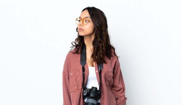 Joven fotógrafo mujer sobre pared blanca mirando hacia el lado