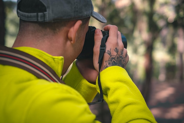 Joven fotógrafo con sombrero trabajando tomando fotos de la naturaleza en el bosque con su cámara