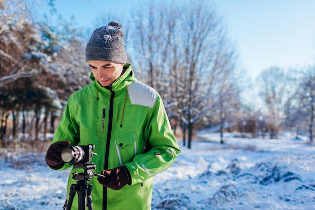 Joven fotógrafo toma fotos del bosque de invierno con cámara y trípode