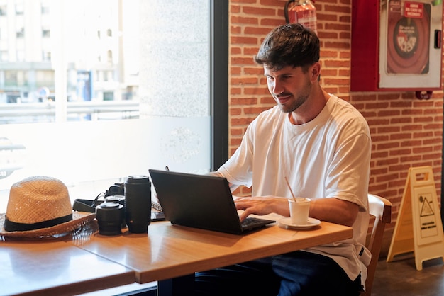 Joven fotógrafo trabaja en una cafetería con su computadora portátil