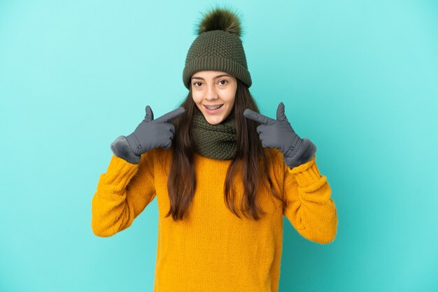 Joven francesa aislada sobre fondo azul con sombrero de invierno dando un pulgar hacia arriba gesto