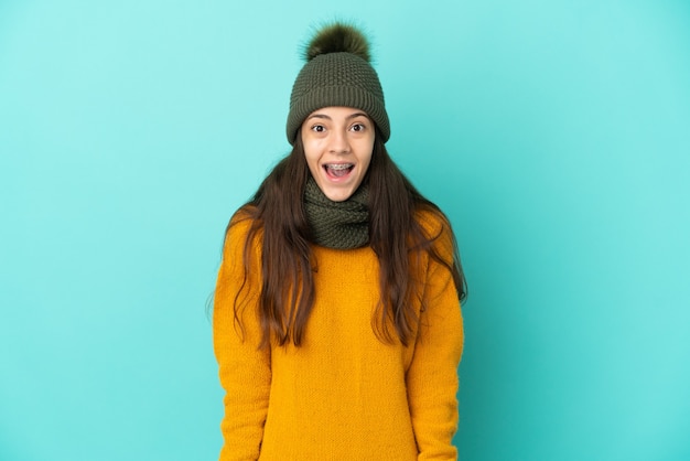 Joven francesa aislada sobre fondo azul con sombrero de invierno con expresión facial sorpresa