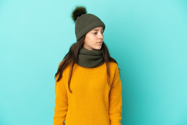 Joven francesa aislada sobre fondo azul con sombrero de invierno mirando hacia el lado