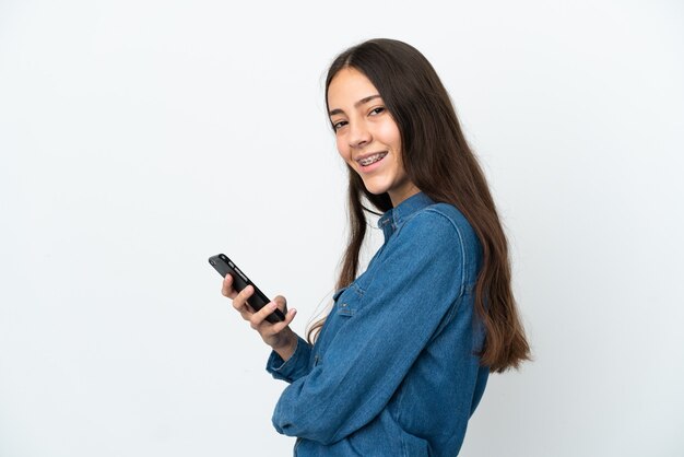 Joven francesa aislada sobre fondo blanco sosteniendo un teléfono móvil y con los brazos cruzados
