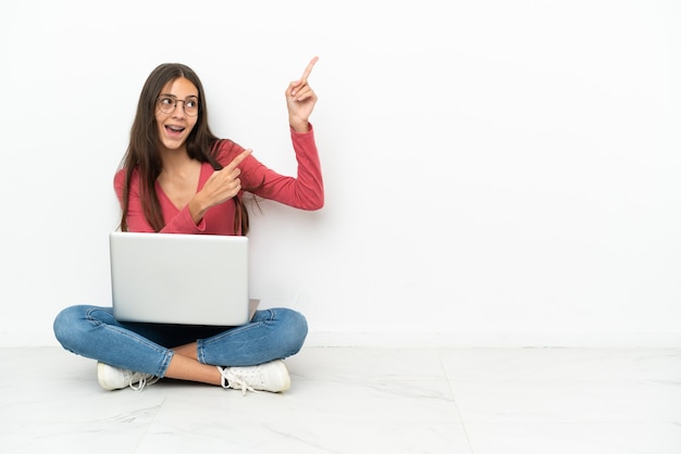 Joven francesa sentada en el suelo con su computadora portátil apuntando con el dedo índice una gran idea