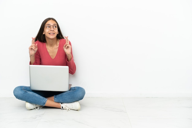 Joven francesa sentada en el suelo con su computadora portátil con los dedos cruzados