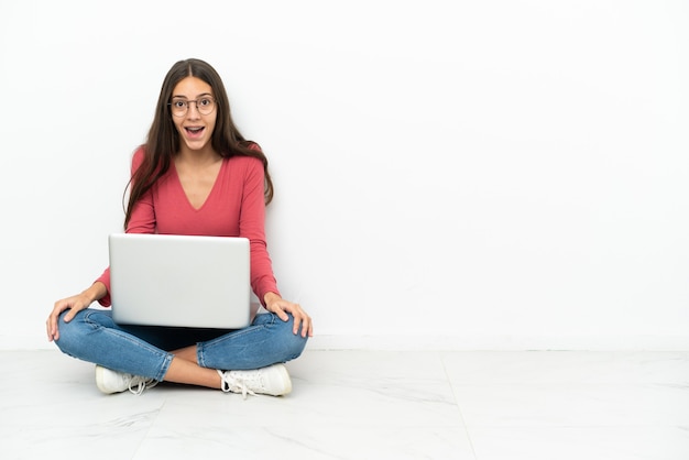 Joven francesa sentada en el suelo con su computadora portátil con expresión facial sorpresa