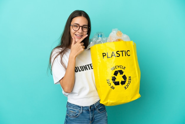 Joven francesa sosteniendo una bolsa llena de botellas de plástico para reciclar feliz y sonriente