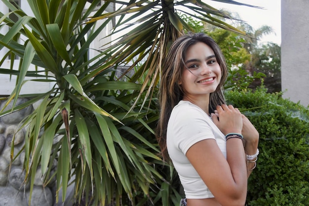 Una joven se para frente a una palmera y sonríe a la cámara.