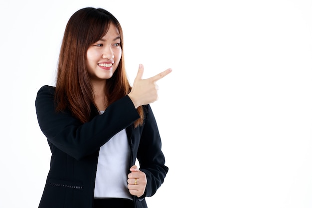 Joven y fresca mirada graduada empresaria asiática en traje posan en gesto publicitario, señalando con el dedo al espacio en blanco para mostrar o presentar bienes y productos. Aislado sobre fondo blanco.