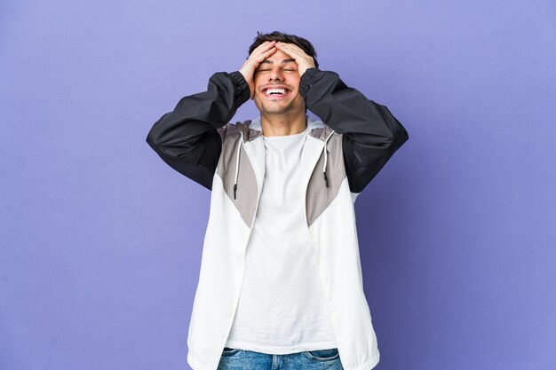 Joven fresco ríe con alegría manteniendo las manos en la cabeza. Concepto de felicidad.