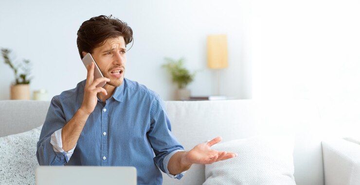 Foto un joven frustrado habla por teléfono con una mirada estresada en su cara mientras está sentado en un sofá