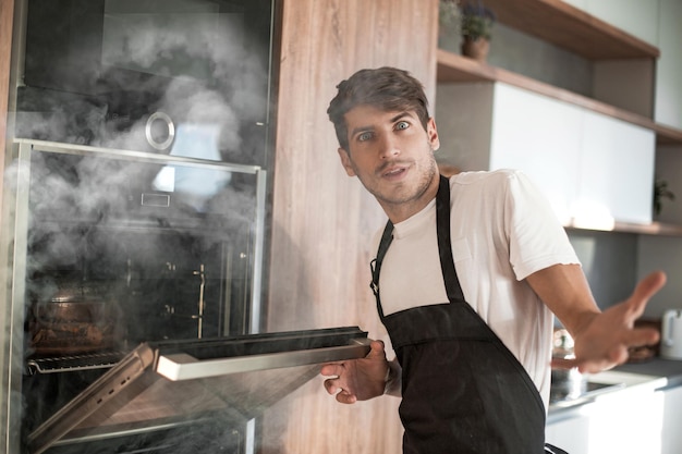 Joven frustrado parado cerca de un horno roto