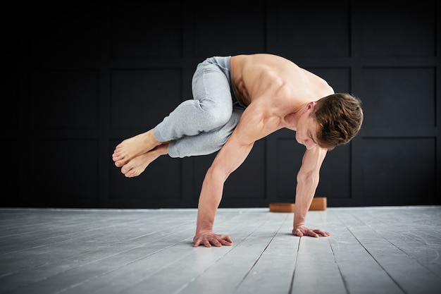 Joven fuerte sin camisa practica yoga en el estudio de yoga