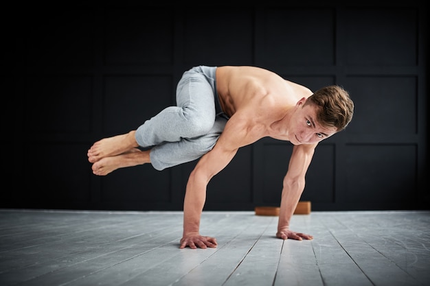 Joven fuerte sin camisa practica yoga en el estudio de yoga