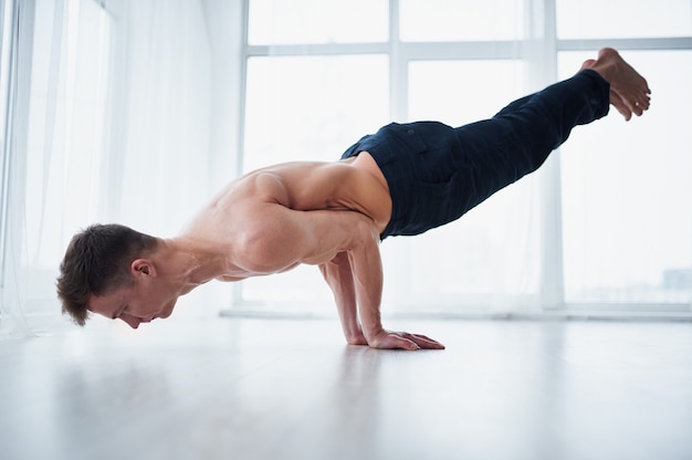 Joven fuerte sin camisa practica yoga en el estudio de yoga