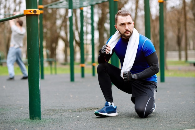 Joven fuerte descansando después de entrenar en un campo deportivo en el verano en la ciudad