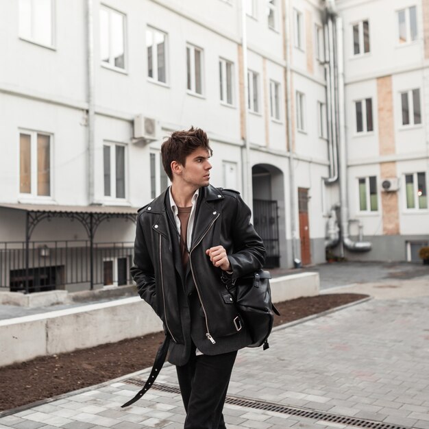 Hombre brutal joven inconformista en ropa casual negra de moda posando en  la ciudad cerca de la carretera. elegante modelo de chico urbano moderno  con una chaqueta de cuero vintage de gran