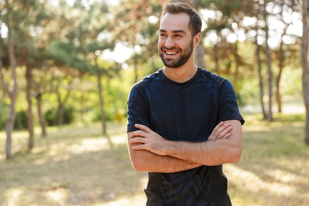 joven fuerte positivo optimista alegre deportes hombre posando al aire libre en la naturaleza parque verde mirando a un lado.