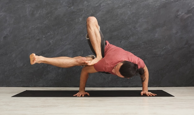 Foto joven fuerte practicando yoga, de pie en pose flexible en las manos sobre la colchoneta en la clase de gimnasia, haciendo ejercicio de equilibrio, espacio de copia