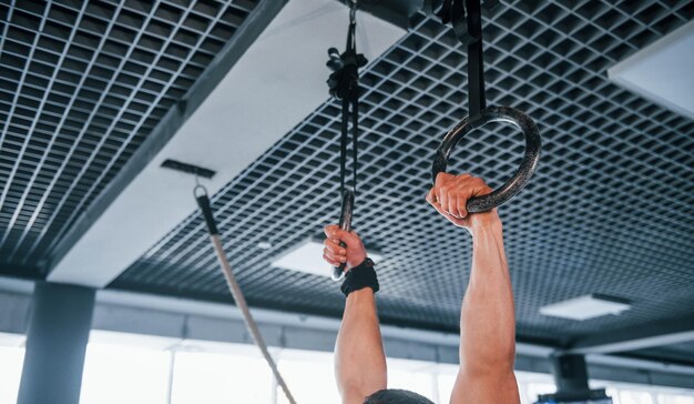 Joven fuerte con ropa deportiva haciendo ejercicios en anillos de gimnasia en el gimnasio