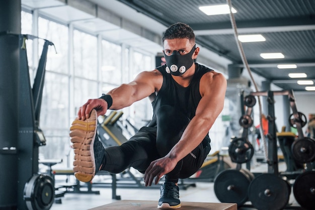 Un joven fuerte con ropa deportiva y una máscara aterradora haciendo flexiones en una pierna en el gimnasio