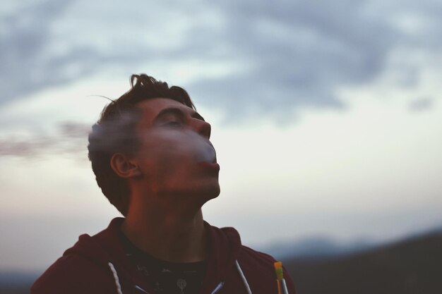 Foto joven fumando un cigarrillo electrónico contra el cielo