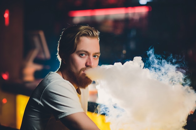 Joven fumando shisha en el restaurante árabe - Hombre exhalando humo inhalando desde una cachimba.