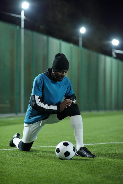 Joven futbolista africano de pie sobre la rodilla en el campo de fútbol