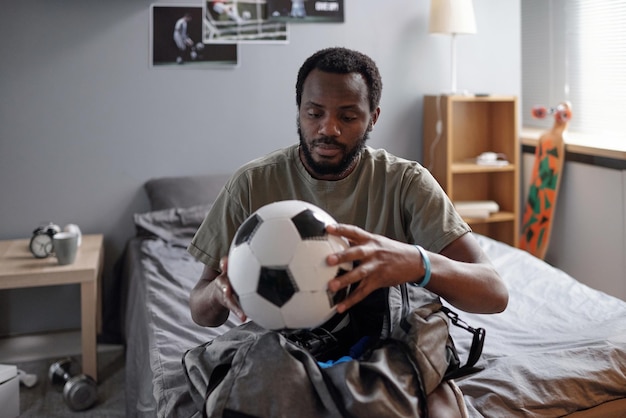 Joven futbolista africano poniendo la pelota en la bolsa