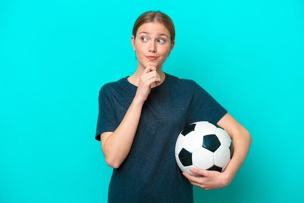 Joven futbolista mujer aislada de fondo azul y mirando hacia arriba