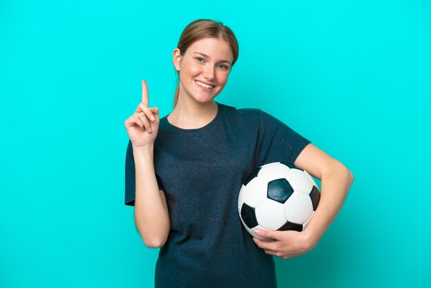 Joven futbolista mujer aislada sobre fondo azul mostrando y levantando un dedo en señal de lo mejor