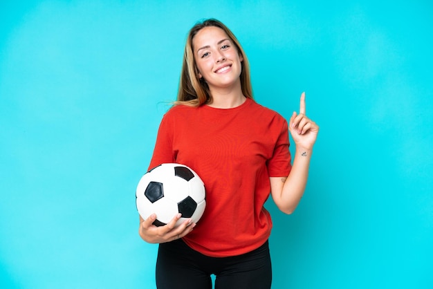 Joven futbolista mujer aislada sobre fondo azul mostrando y levantando un dedo en señal de lo mejor