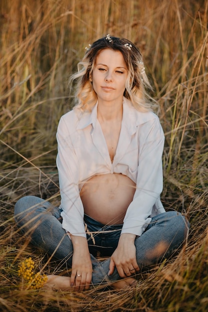 Una joven futura madre en el tercer trimestre del embarazo está sentada en un claro entre las plantas de cereales El concepto de futura maternidad