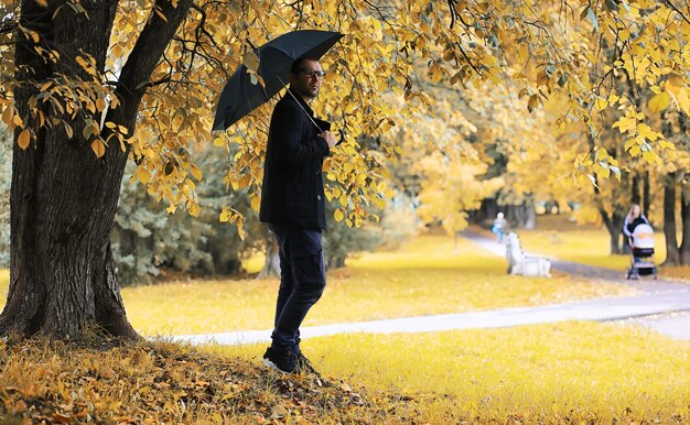 Un joven con gafas camina en el parque con un paraguas durante la lluvia.