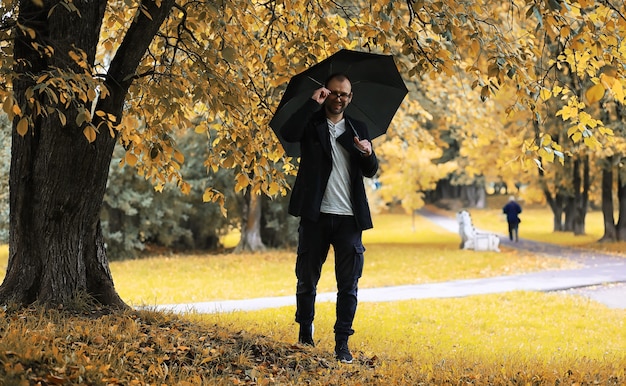 Un joven con gafas camina en el parque con un paraguas durante la lluvia.