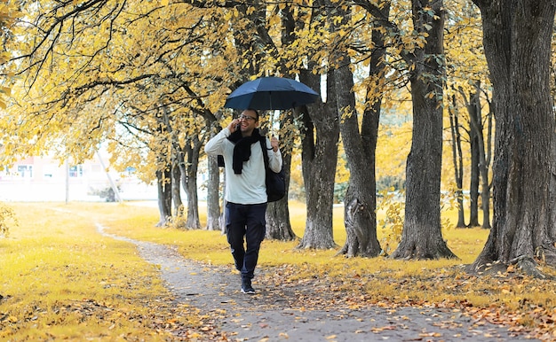 Un joven con gafas camina en el parque con un paraguas durante la lluvia.