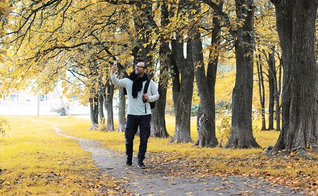 Un joven con gafas camina en el parque con un paraguas durante la lluvia.