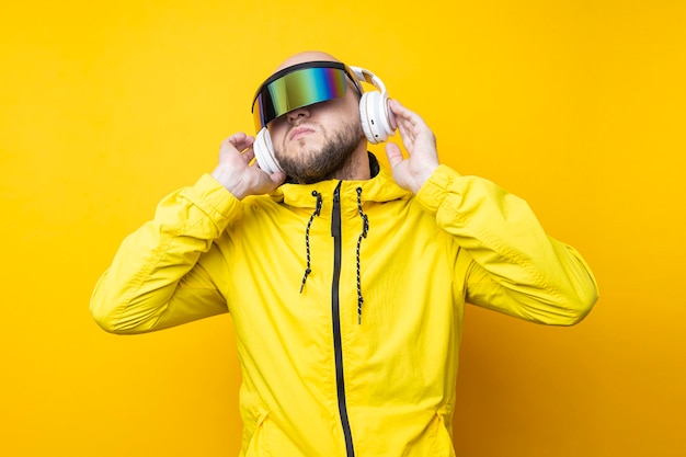 Joven con gafas cyberpunk en una chaqueta amarilla con auriculares en un fondo amarillo