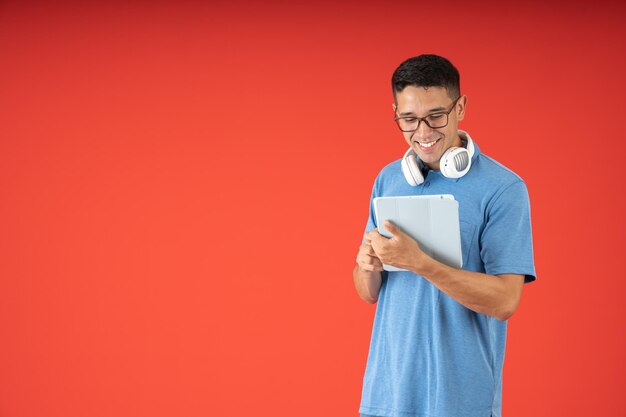 Joven con gafas feliz y sonriente usando una tableta digital y auriculares