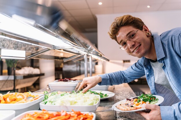 Joven con gafas y piercings tomando comida de un autoservicio