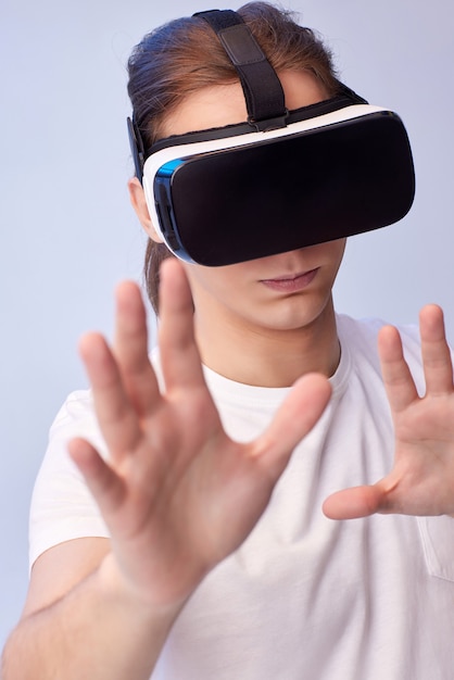 Joven con gafas de realidad virtual jugando videojuegos sobre fondo azul.