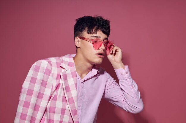 Un joven con gafas rosas, chaqueta rosa, posando en el estudio, fondo rosa inalterado.