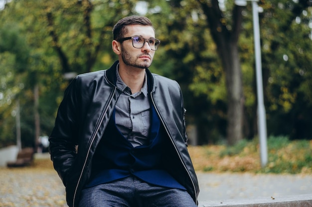 un joven con gafas se sienta en un banco