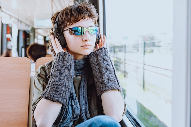 Un joven con gafas de sol y un par de gafas de sol se sienta en un tren y escucha música.