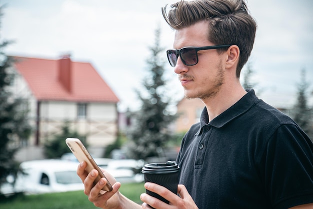 Un joven con gafas de sol con teléfono inteligente y café en la ciudad.