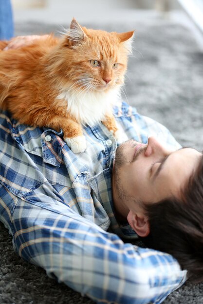 Joven con gato esponjoso acostado en una alfombra