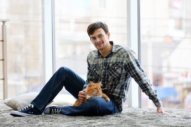 Joven con gato esponjoso sentado en una alfombra