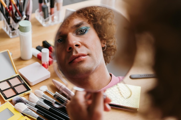 Foto joven gay confiado mirando su reflejo en el espejo mientras se aplica maquillaje