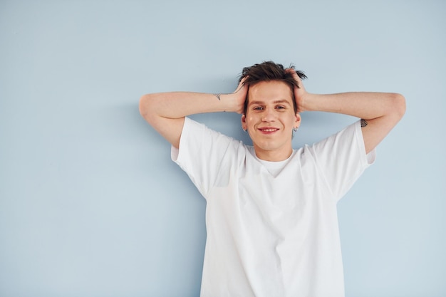 Joven gay está parado en el estudio y posando para una cámara con una camisa blanca casual